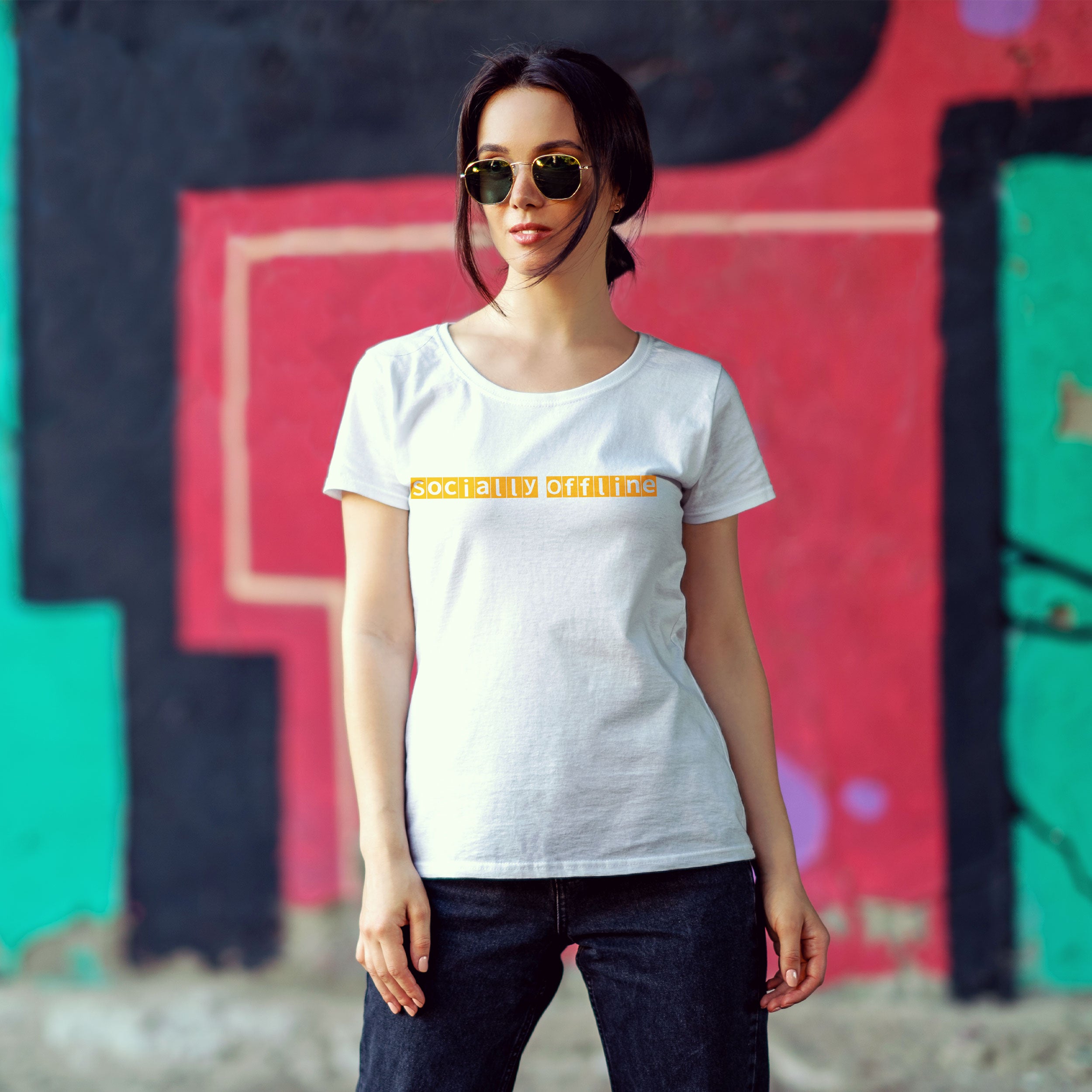 Woman wearing a white t-shirt with yellow text in front of a colorful graffiti wall.